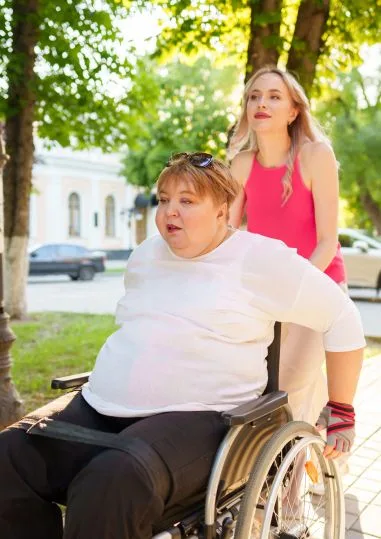A support worker assisting a participant who uses a wheelchair on a tree-lined street
